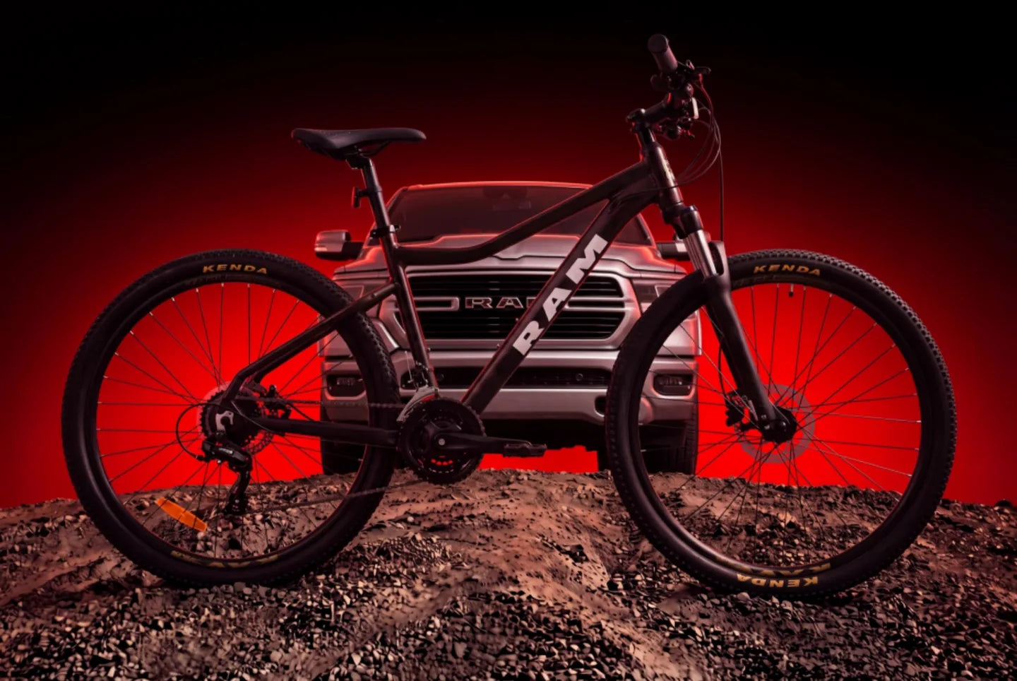 Bicicleta RAM negra de perfil frente a una camioneta RAM sobre un montículo de tierra